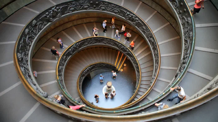 Visitors descend the double spiral ramp of the Vatican Museums staircase with its bronze balustrade.