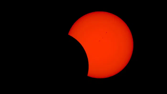 Partial solar eclipse, the moon carving a dark bite from an orange sun dotted with sunspots.