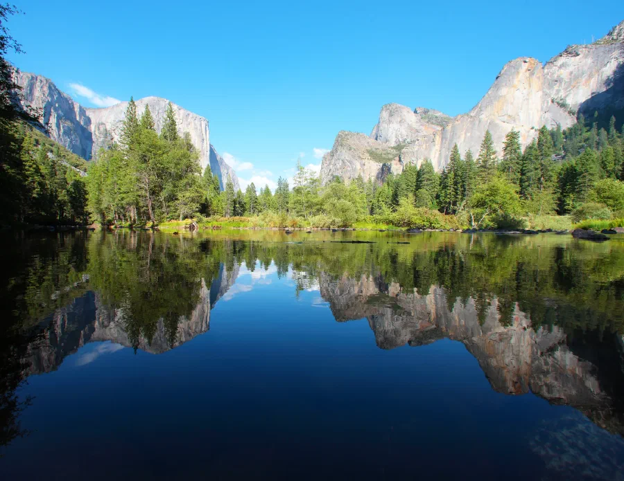 Granite cliffs and pines mirror perfectly in a calm river under a deep blue sky.