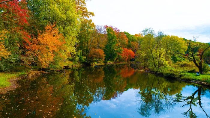 Autumn trees in red, orange, and gold line a still river that mirrors them.